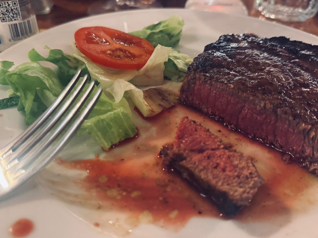 Perfectly grilled thick-cut steak served with fresh salad and tomato on a white plate at a local restaurant during a motorcycle tour