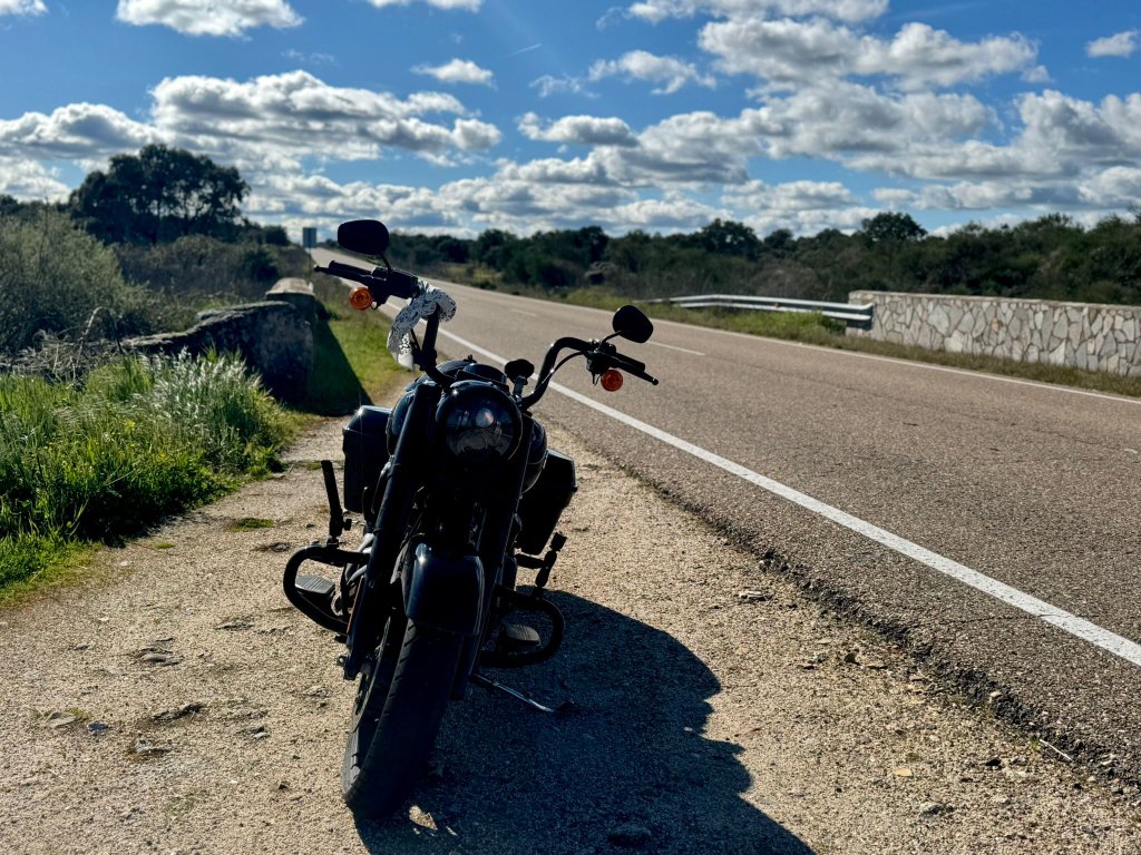 Black Harley Davidson motorcycle parked on the verge of an empty Spanish road with scrubland and blue skies with white clouds stretching to the horizon