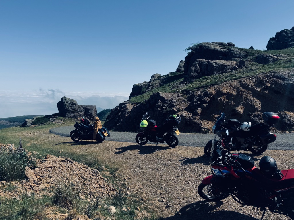 Three Wild Roads motorcycles on rocky mountain pass road above cloud inversion — Pyrenees May 2026