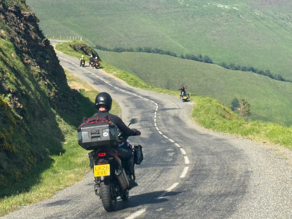 Wild Roads group descending narrow mountain road in Pyrenees — shot from above — May 2026
