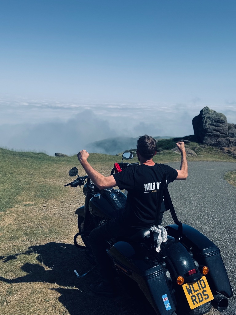 Wild Roads rider on Harley Road King arms raised above cloud inversion — Wild Roads T-shirt — Pyrenees May 2026
