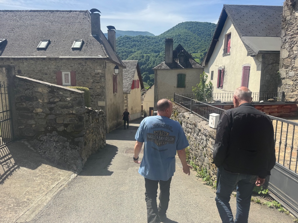 Two Wild Roads riders walking through narrow stone lane in Montory village — French Basque Country — May 2026
