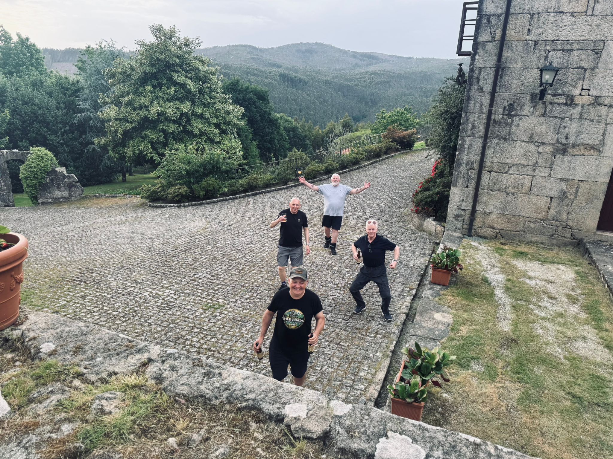 Wild Roads crew in cobbled courtyard at Galician farmhouse — beers and smiles