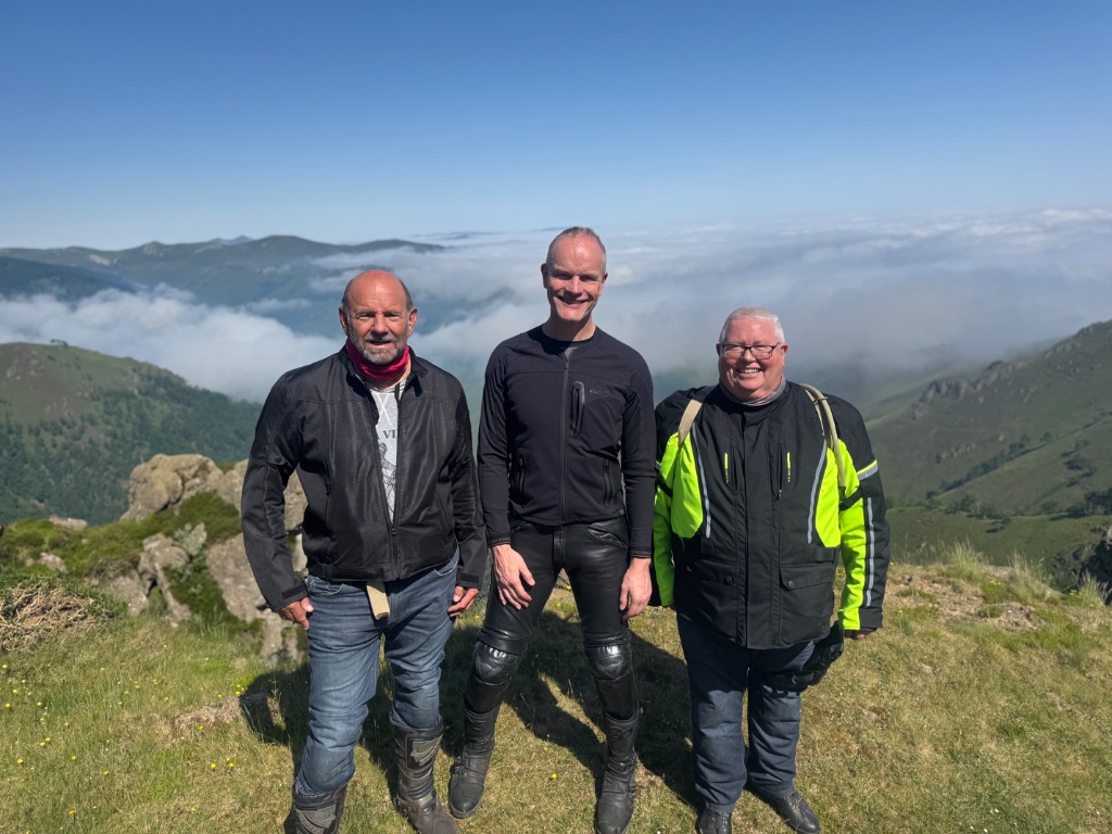 Three Wild Roads riders on summit above cloud inversion — Pyrenean mountains — May 2026