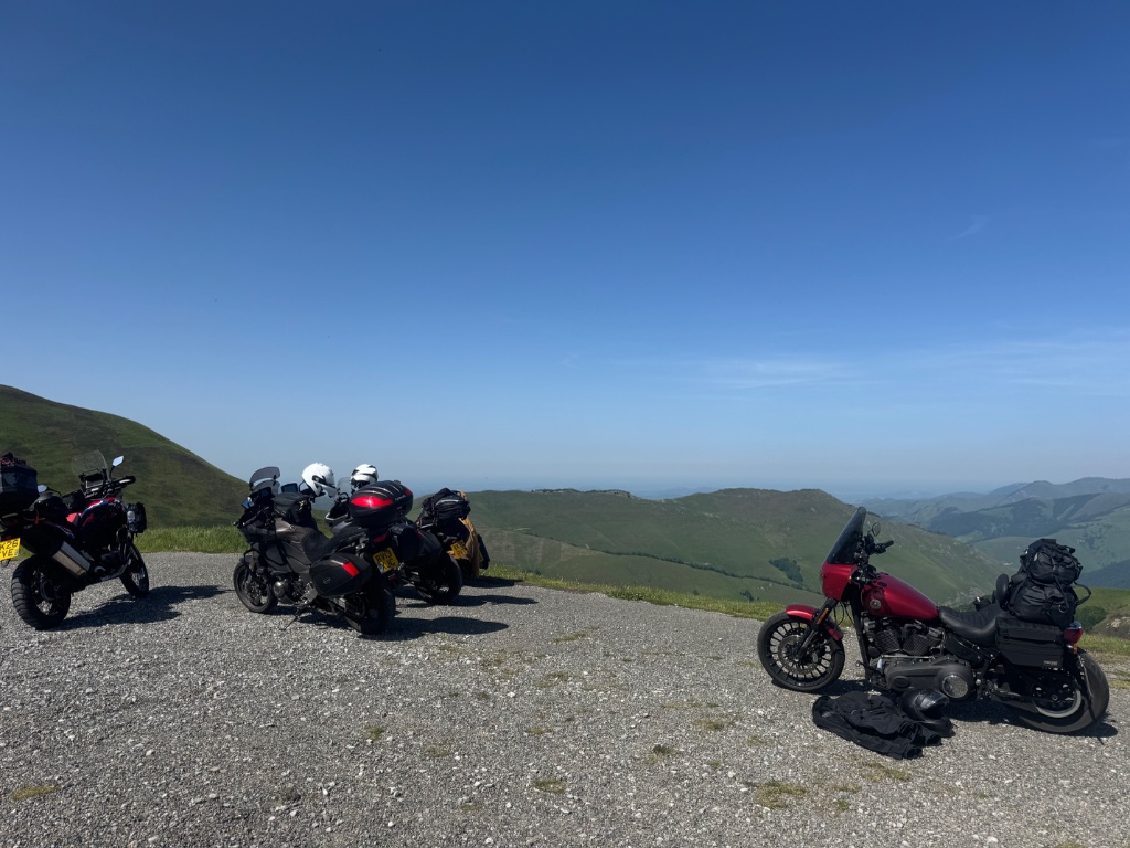 Wild Roads bike fleet at high mountain viewpoint — Pyrenees ridgeline — Harley-Davidson and adventure bikes May 2026