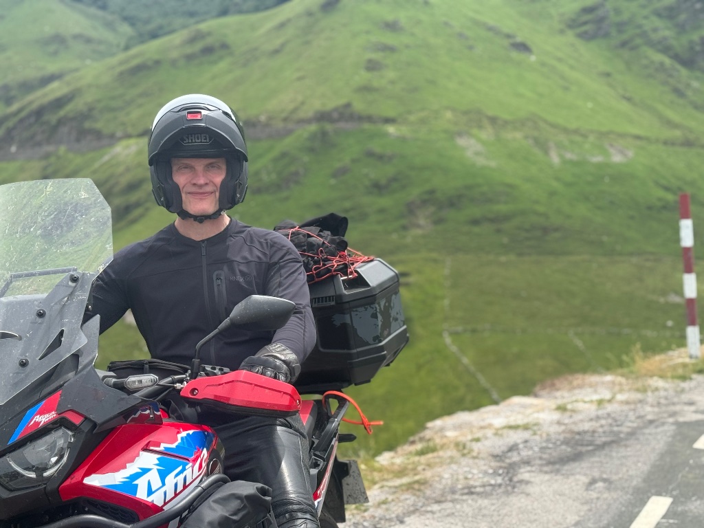 Rider on Honda Africa Twin at high Pyrenean col Shoei helmet green mountains — Picos & Pyrenees May 2026