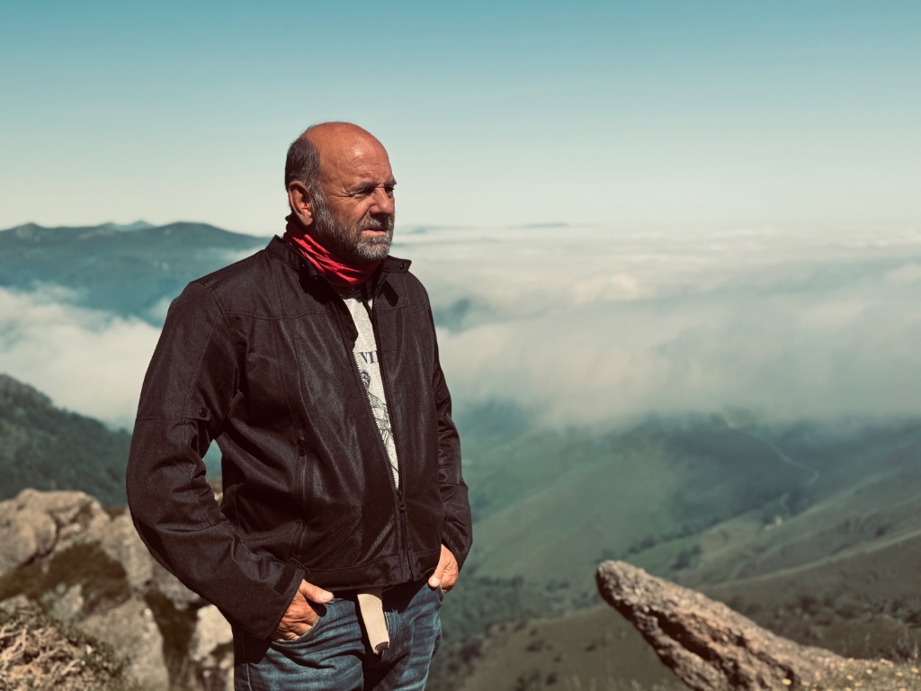 Wild Roads rider standing on rocky summit gazing over cloud inversion in valley below — Pyrenees May 2026