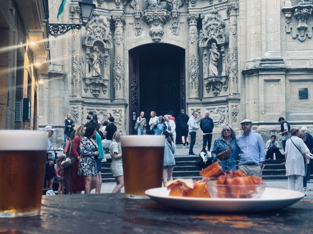 Pintxos and beer on barrel table outside bar — Basilica de Santa Maria del Coro San Sebastian old town — Wild Roads May 2026
