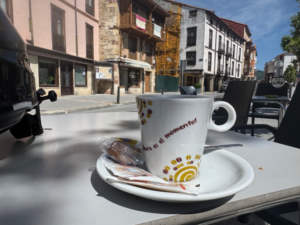 Spanish coffee cup Ahora es el momento on café terrace — Cervera de Pisguera — Wild Roads motorcycle tour May 2026