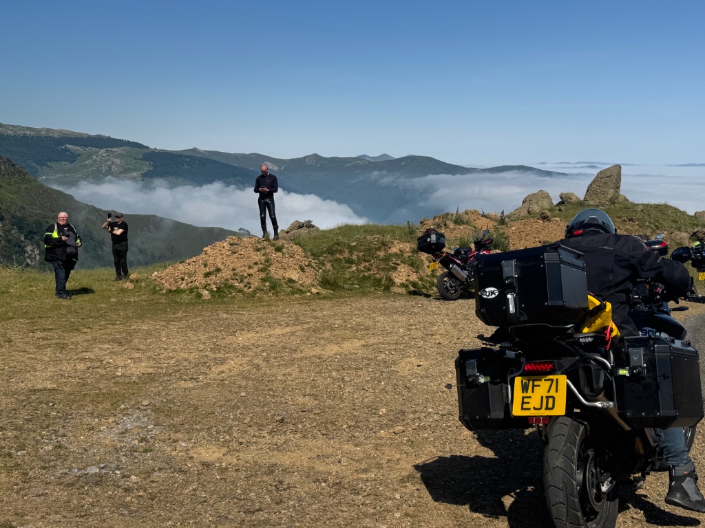 Wild Roads riders on rocky outcrop above cloud inversion — bikes parked behind — Pyrenees May 2026